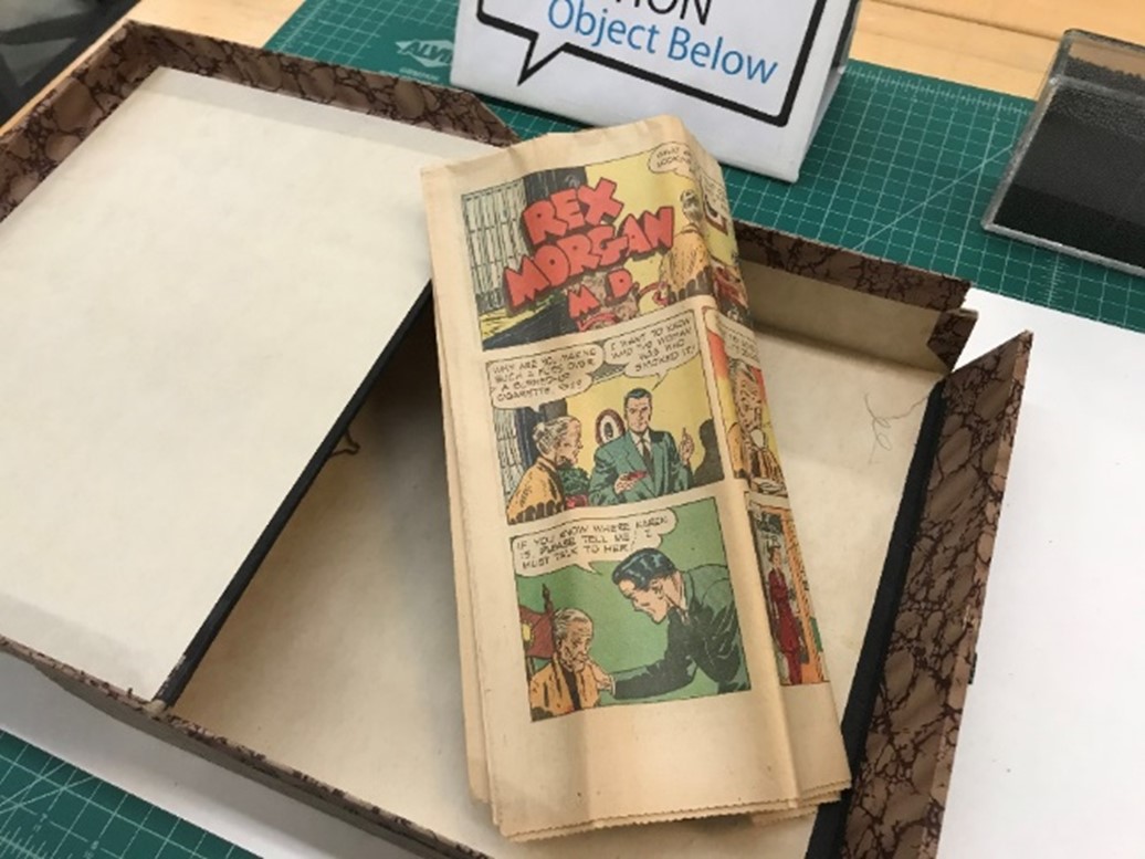 Photograph of newspaper comics page folded up and resting on open box 