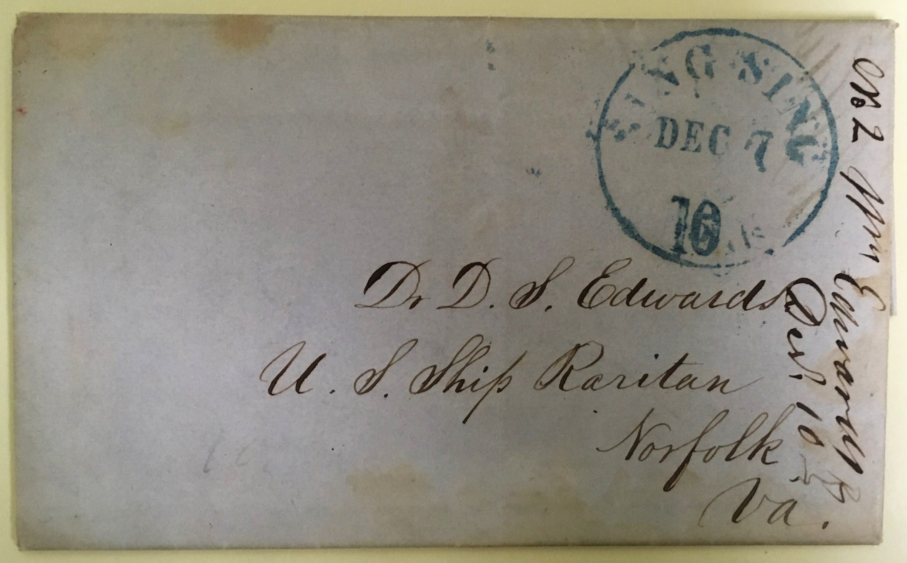 Image of old envelope that has faded to a dull grey color. Delicate cursive adorns the envelope, and a green circular cancel stamp.