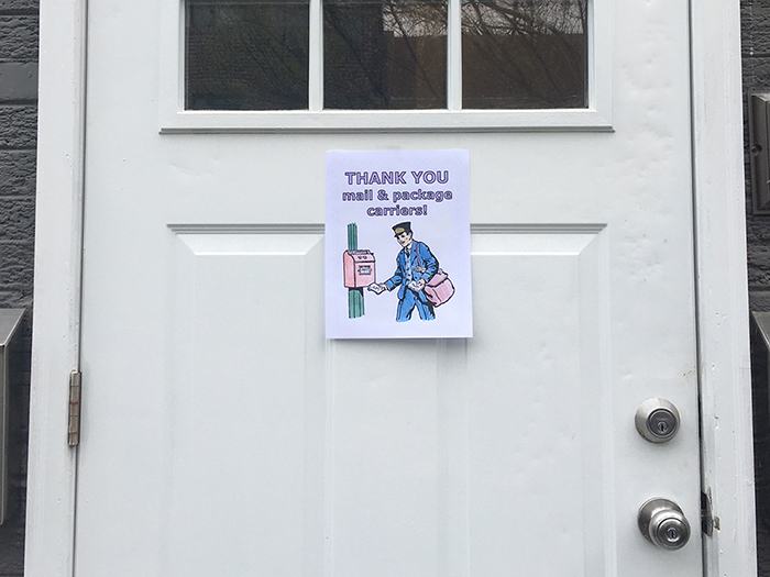 A white door that has a picture of a coloring book page thanking postal workers taped to it.