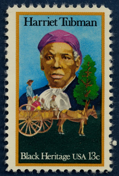 a 13-cent stamp with Harriet Tubman, an African American woman, on it. She is shown in portrait, facing the viewer, and wearing a purple hair covering. In the foreground there is an image of four African American adults in a wagon being pulled by horses.