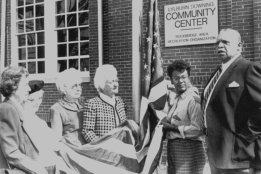 Six people dedicating a flag in front of a community center