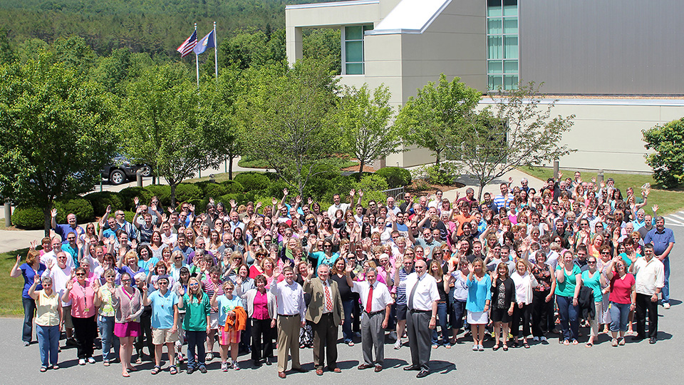A large group of employees posing for an outdoor photo in front of their building