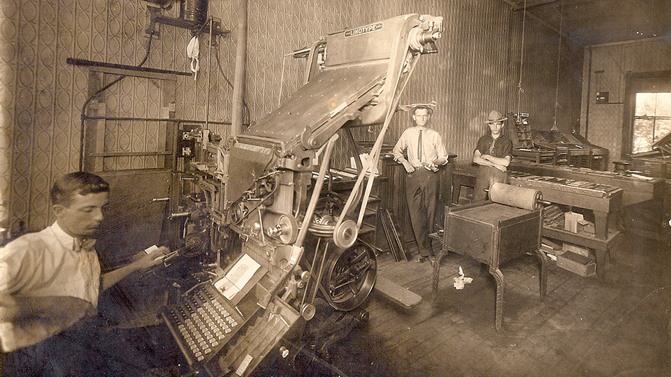 Newspaper employees working with a linotype and a proof press, circa 1916.