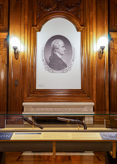 Hamilton exhibition gallery with wood paneling and a portrait of Hamilton above a fireplace