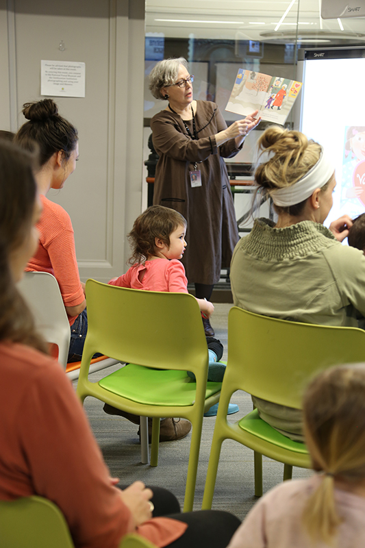 An adult standing and reading a children’s book to an audience.